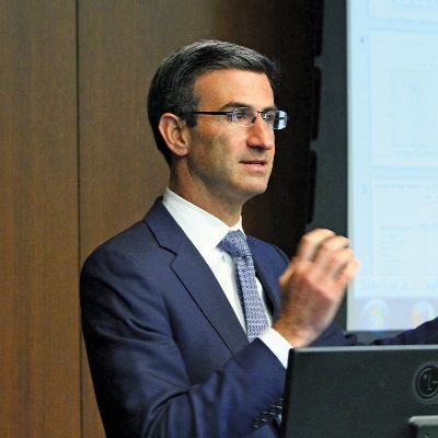 He is standing next to slide show as he is speaking.